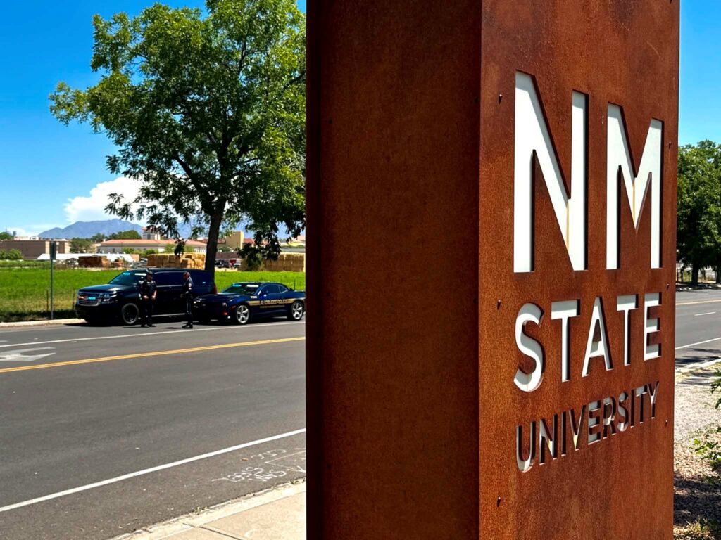New Mexico State University sign in front of a street where a police car stopped another vehicle.