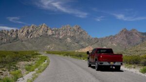 Red truck driving on a road with the Organ Mountains in the background.