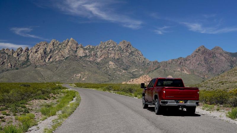 Red truck driving on a road with the Organ Mountains in the background.