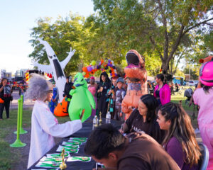 People dressed in costumers talking to person at a table outdoors.