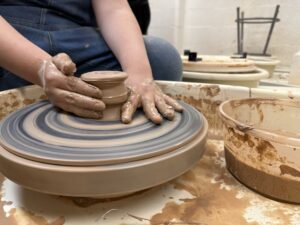A pair of hands shape a clay piece on a pottery wheel.