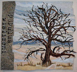 Textile artwork of a stark, leafless tree , with blue-gray sky, grasses, and a patterned vertical border.
