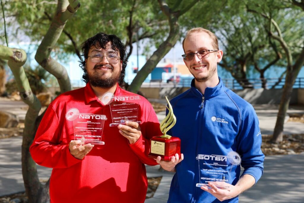 Two men standing in front of trees holding trophies.