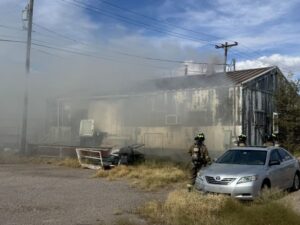 Firefighters outside a building with smoke surrounding it.