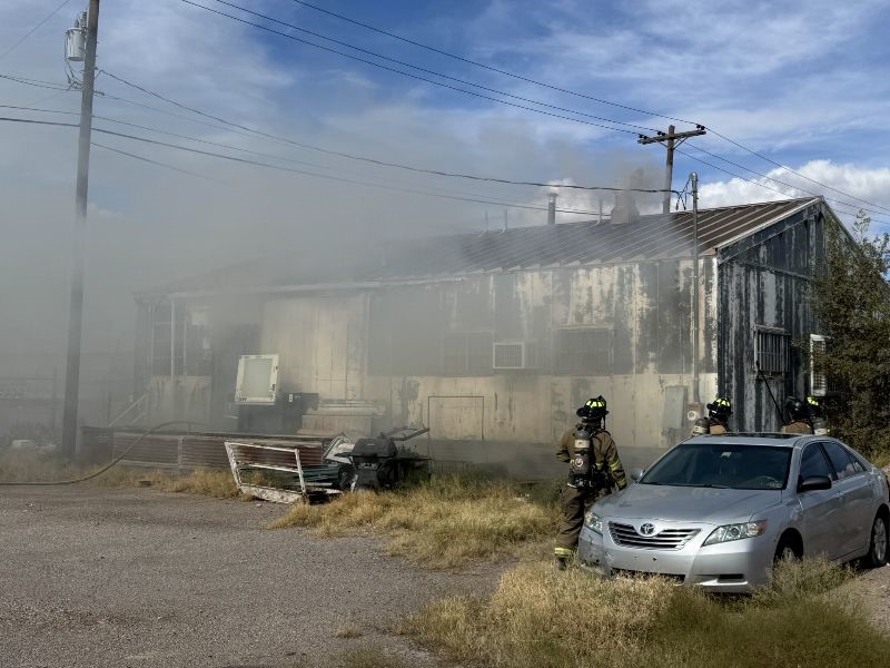 Firefighters outside a building with smoke surrounding it.