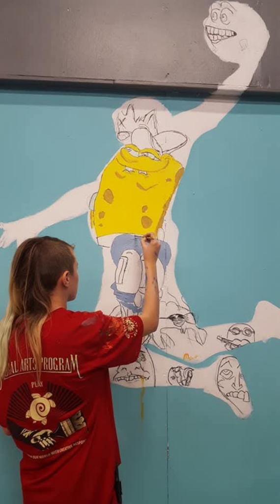 Teen painting on human shape projected on a wall. Shape is of person dunking a basketball.