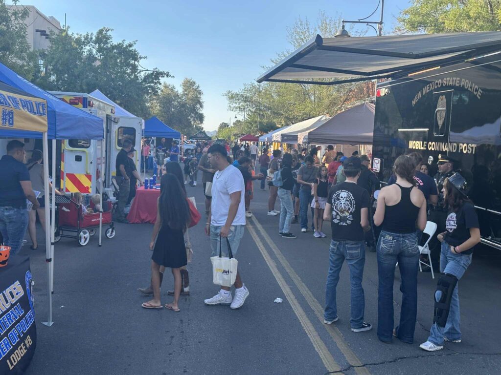 People gathered in front of vendors set up on a street with trees in the background.