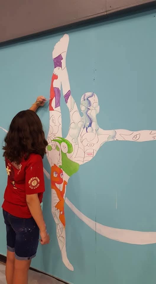 Female teen painting a shape of person in a gymnastics shape projected on a wall.