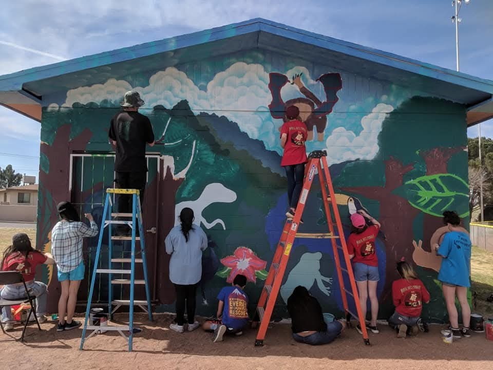 Group of teens painting mural on side of small building.