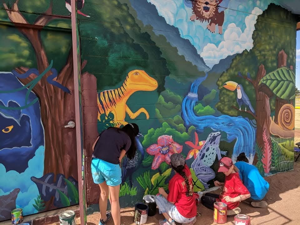 Close up of four teens painting mural on wall.