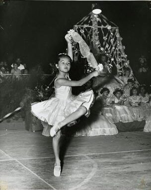 A black and white picture of a young ballerina dancing in front of a crowd.
