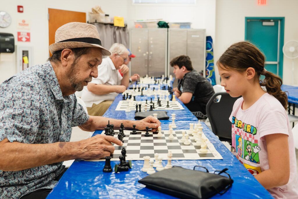 People sit along a table playing chess.