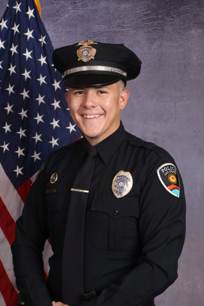 A police officer in uniform with the U.S. flag in the background.